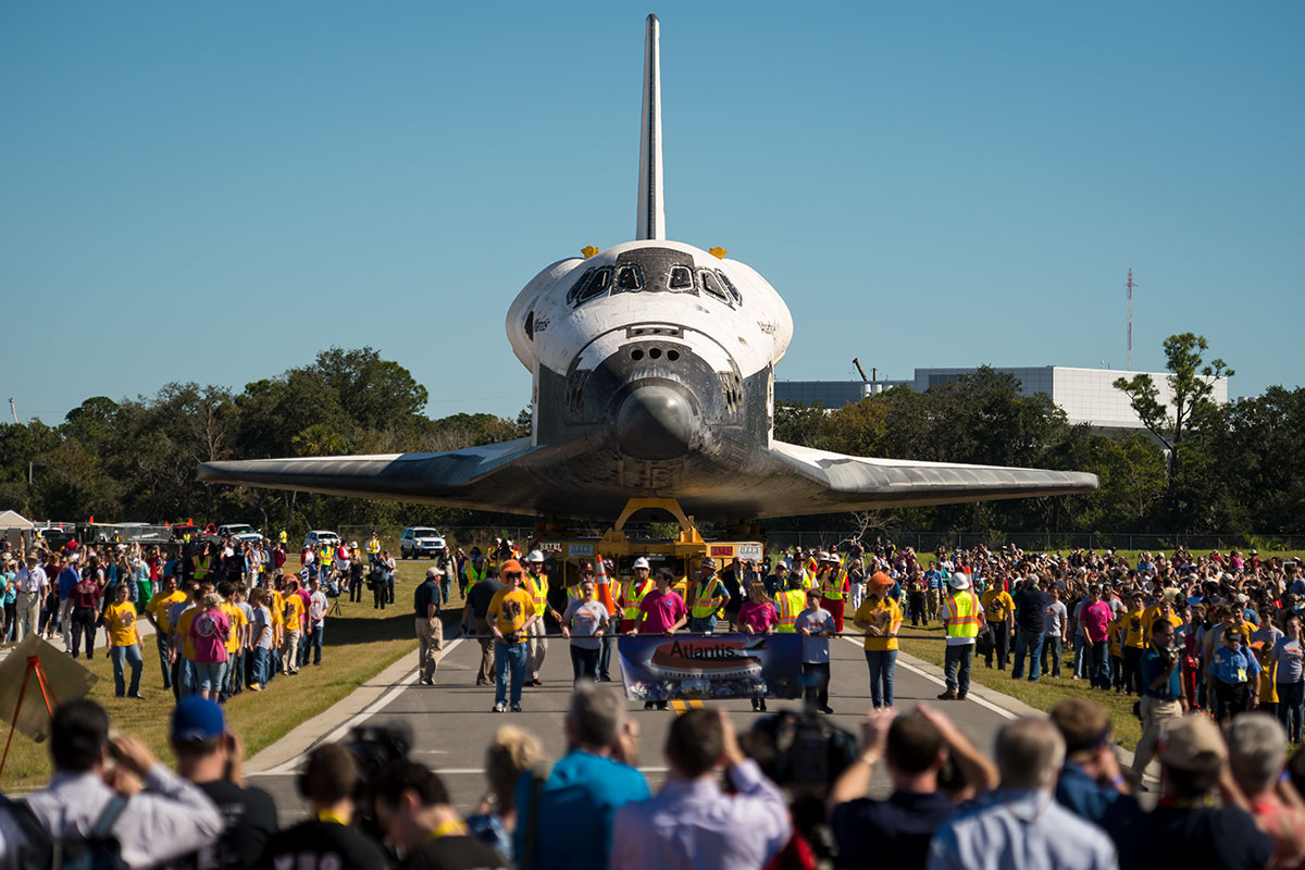 Photo of space shuttle Atlantis being brought to the Kennedy Space Center while a crowd greets it at its new exhibit.