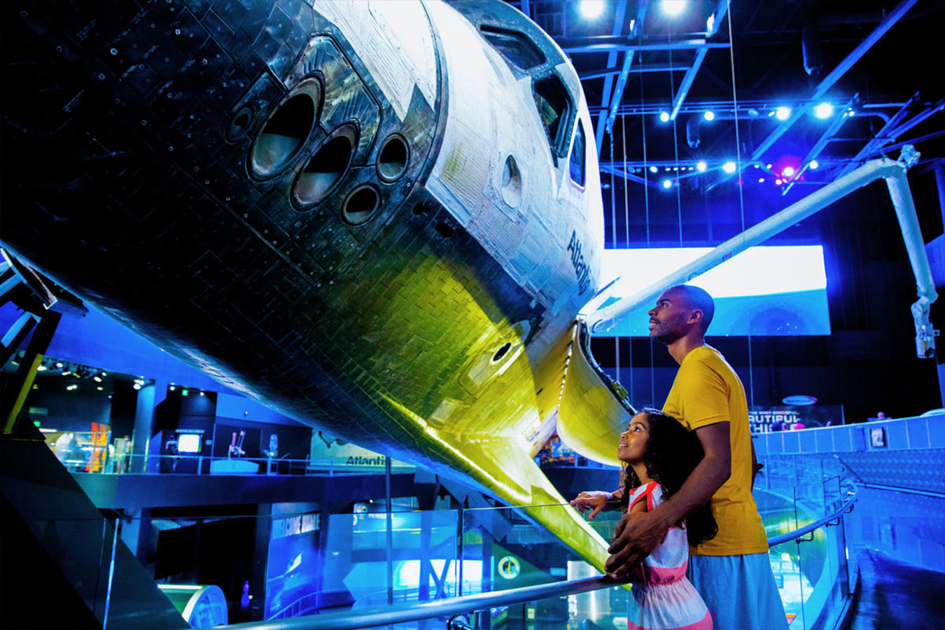Father and daughter look up at the Space Shuttle Atlantis Orbiter on display with payload bay doors open at the Kennedy Space Center Visitor Complex.