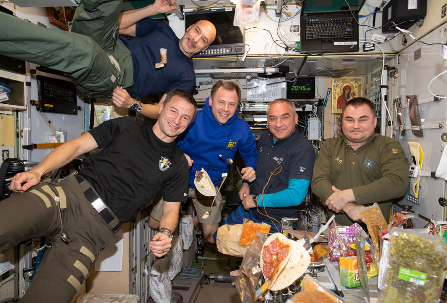 Five members of Expedition 60 eating dinner inside the Zvezda service module. Top is Luca Parmitano of the European Space Agency. From left to right: NASA astronauts Andrew Morgan and Nick Hague, Roscosmos cosmonauts Alexander Skvortsov and Aleksey Ovchinin (Aug. 2, 2019).