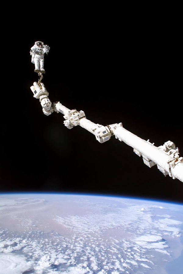 Astronaut Stephen K. Robinson, STS-114 mission specialist, is anchored to the extended ISS’s Canadarm-2 during a spacewalk to repair the Control moment Gyroscopes.