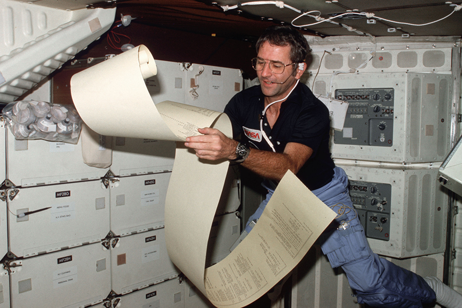 Astronaut Richard H. Truly, STS-2 pilot, peruses some teleprinter copy, floating partially about the middeck area of NASA’s space shuttle Columbia.