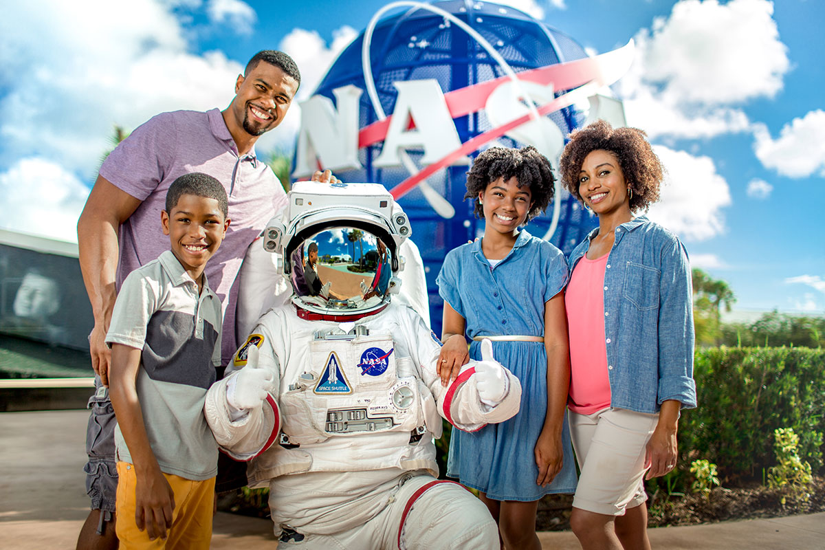 Family poses for a photo with an astronaut in front of the NASA meatball at Kennedy Space Center Visitor Complex.