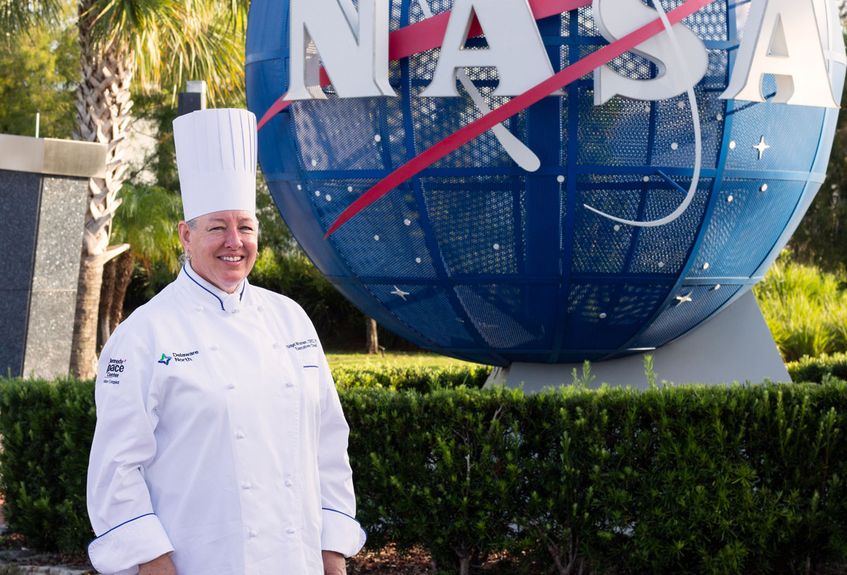 Executive Chef Gidget standing in front of NASA globe at Kennedy Space Center Visitors Complex
