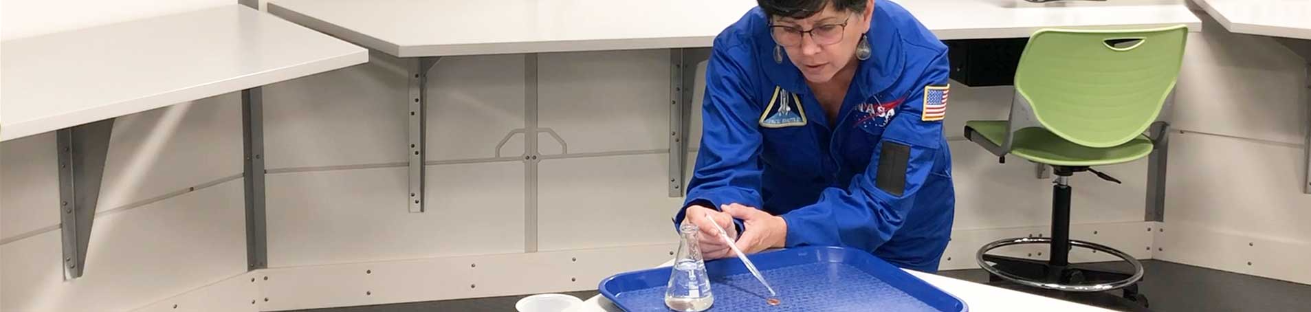 A Kennedy Space Center Visitor Complex educator is performing a water tension experiment.
