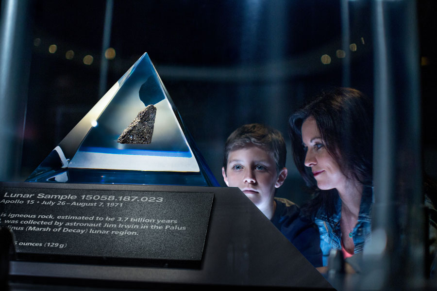 Mãe e filho olham com admiração para a Pedra da Lua em exposição no Apollo/Saturn V Center